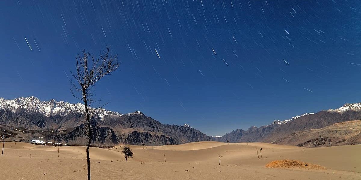 Star trails over the cold desert dunes and snow peaks, Skardu