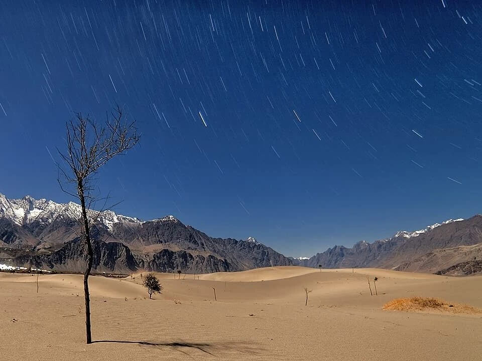 Star trails over the cold desert dunes and snow peaks, Skardu