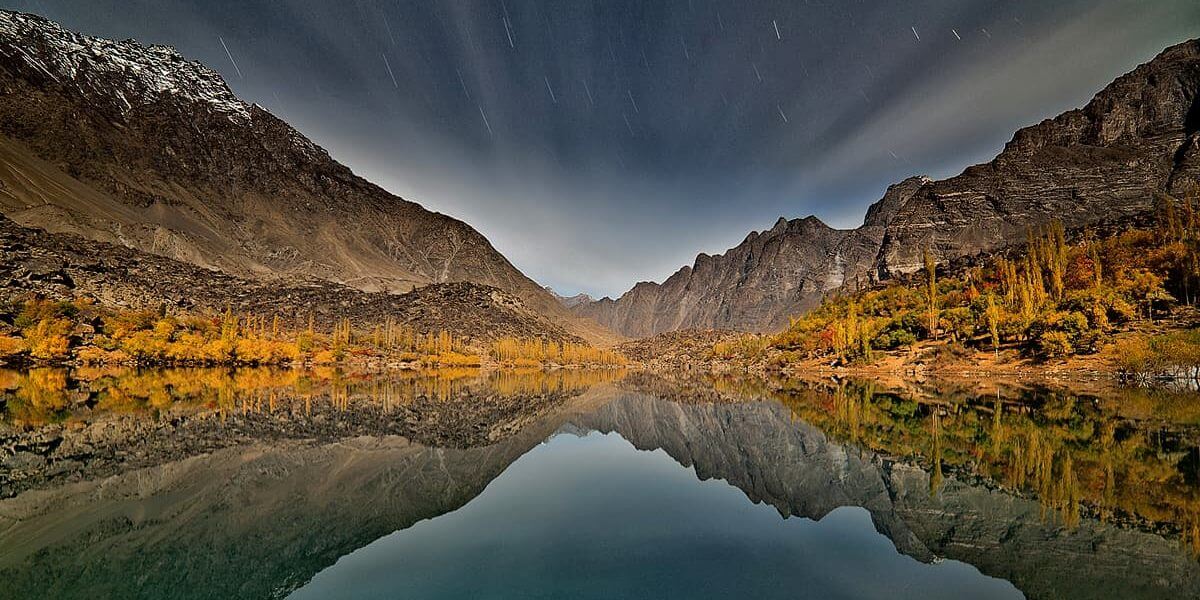 Mountain lake reflecting autumn poplars under star trails, Skardu
