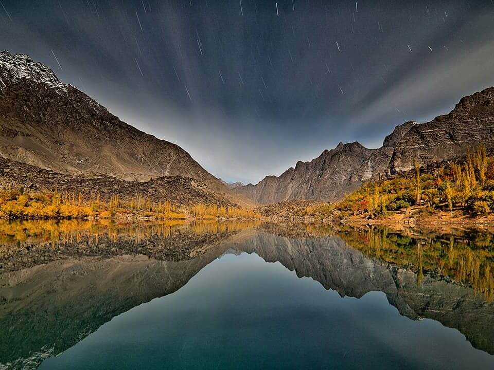 Mountain lake reflecting autumn poplars under star trails, Skardu