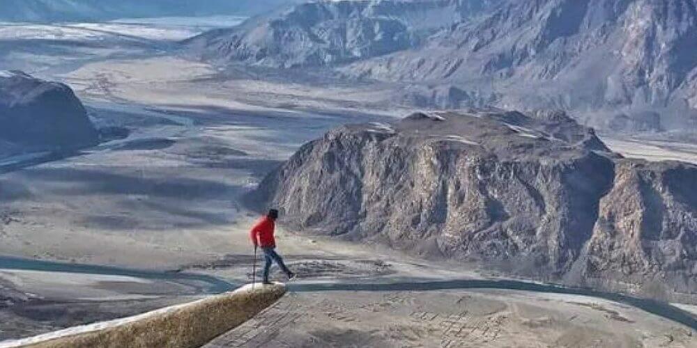 Walker on a rock ledge above the Indus and the Skardu valley in winter