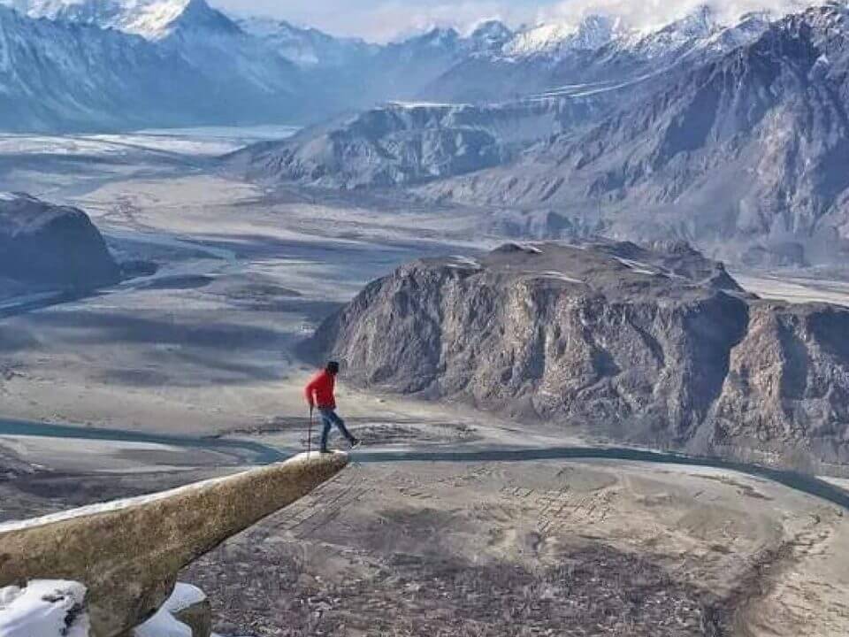 Walker on a rock ledge above the Indus and the Skardu valley in winter